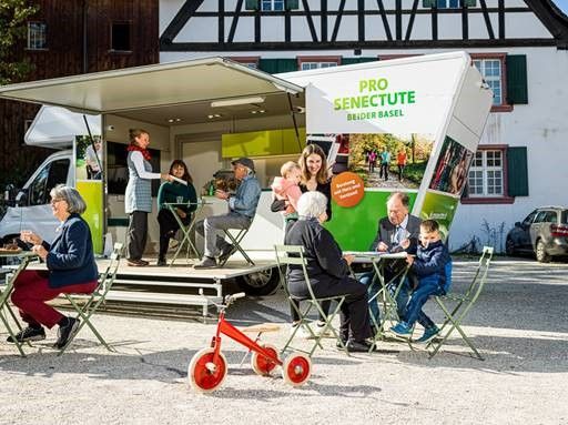 Vor Infobus unterhalten sich Personen unterschiedlichen Alters und nehmen an Aktivitäten teil.