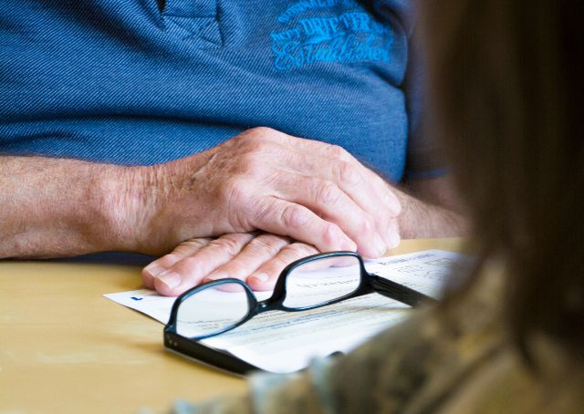 Steuererklärung und Brille liegen neben den gefalteten Händen eines älteren Mannes.