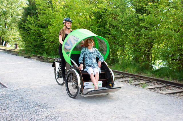 Seniorin und junge Frau machen einen Ausflug in der Natur mit der E-Rikscha.