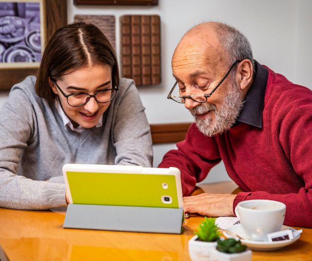Eine Mitarbeiterin des Digital Cafés hilft einem Kunden mit seinem Tablet.