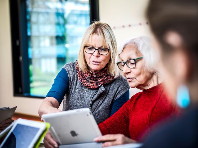 Eine interessierte Kundin mit einem iPad hört der Kursleiterin der digitalen Medien aufmerksam zu.