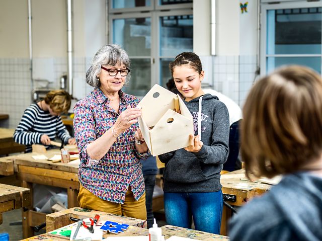 Konzentrierte Seniorin im Freiwilligeneinsatz hilft Primarschulkind bei Werkarbeit aus Holz.