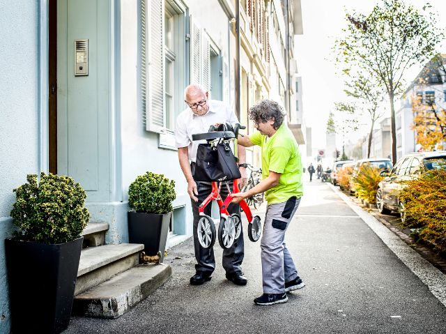 Berater zeigt einem Kunden draussen wie der Rollator zusammengeklappt werden kann.