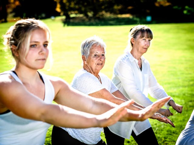 Drei Kursteilnehmerinnen unterschiedlichen Alters nehmen an einer Meditationsstunde in einem Park teil.