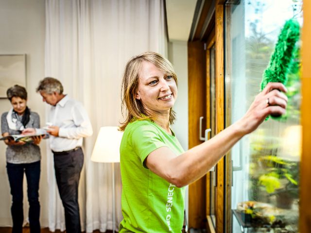 Mitarbeiterin unterstützt ein älteres Ehepaar mit einer Fensterreinigung bei ihnen zuhause.
