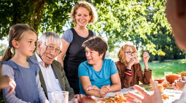 Ältere und junge Menschen im Park unterhalten sich am Tisch.